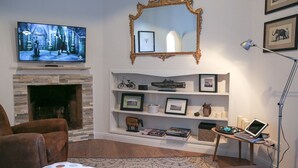 A living room with a fireplace, a television mounted above it, a bookshelf with various items, and a laptop on a side table. - Pandolfini Suite (Florence)
