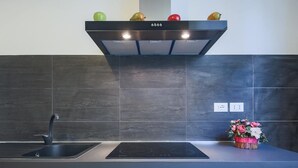 A modern kitchen with a black range hood, a stainless steel sink, and a black induction cooktop. - Pandolfini Suite (Florence)