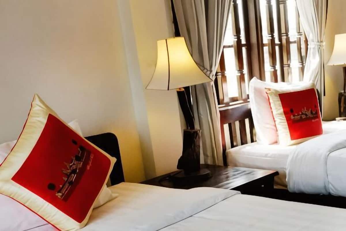 A hotel room with two beds, a nightstand, a lamp, and a window with curtains.