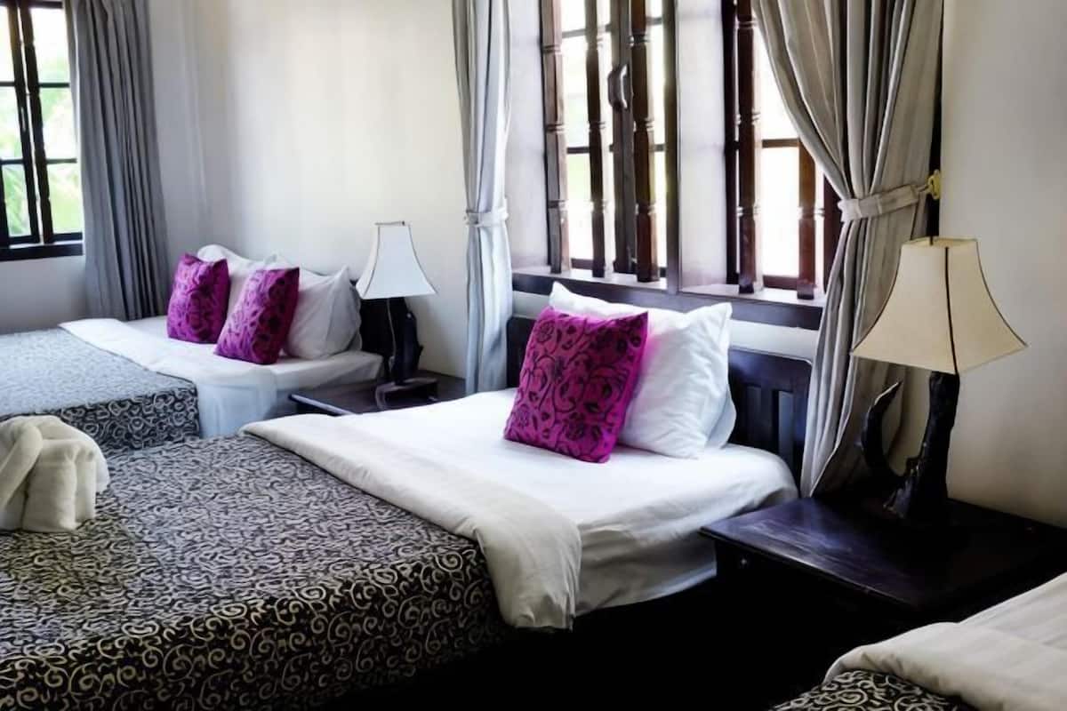 A hotel room with two beds, a nightstand, a lamp, and a window with curtains.