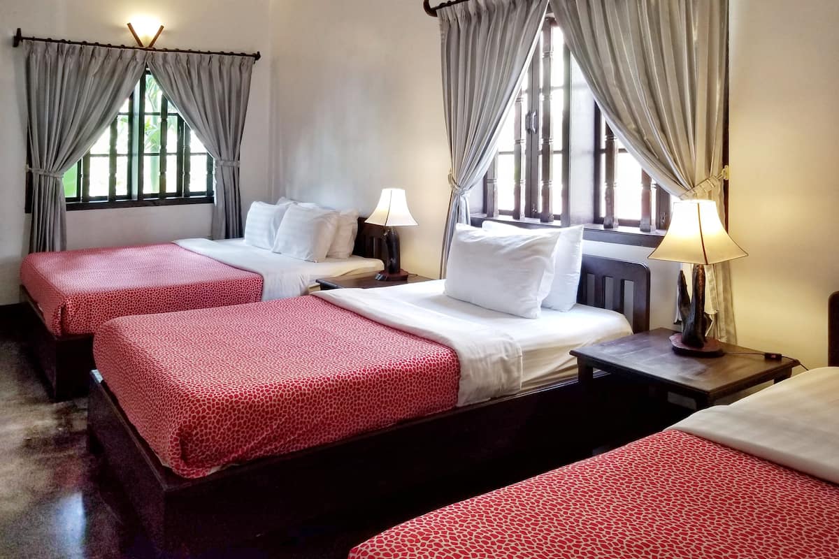 A hotel room with three beds, each with a red patterned bedspread, white pillows, and a bedside lamp.