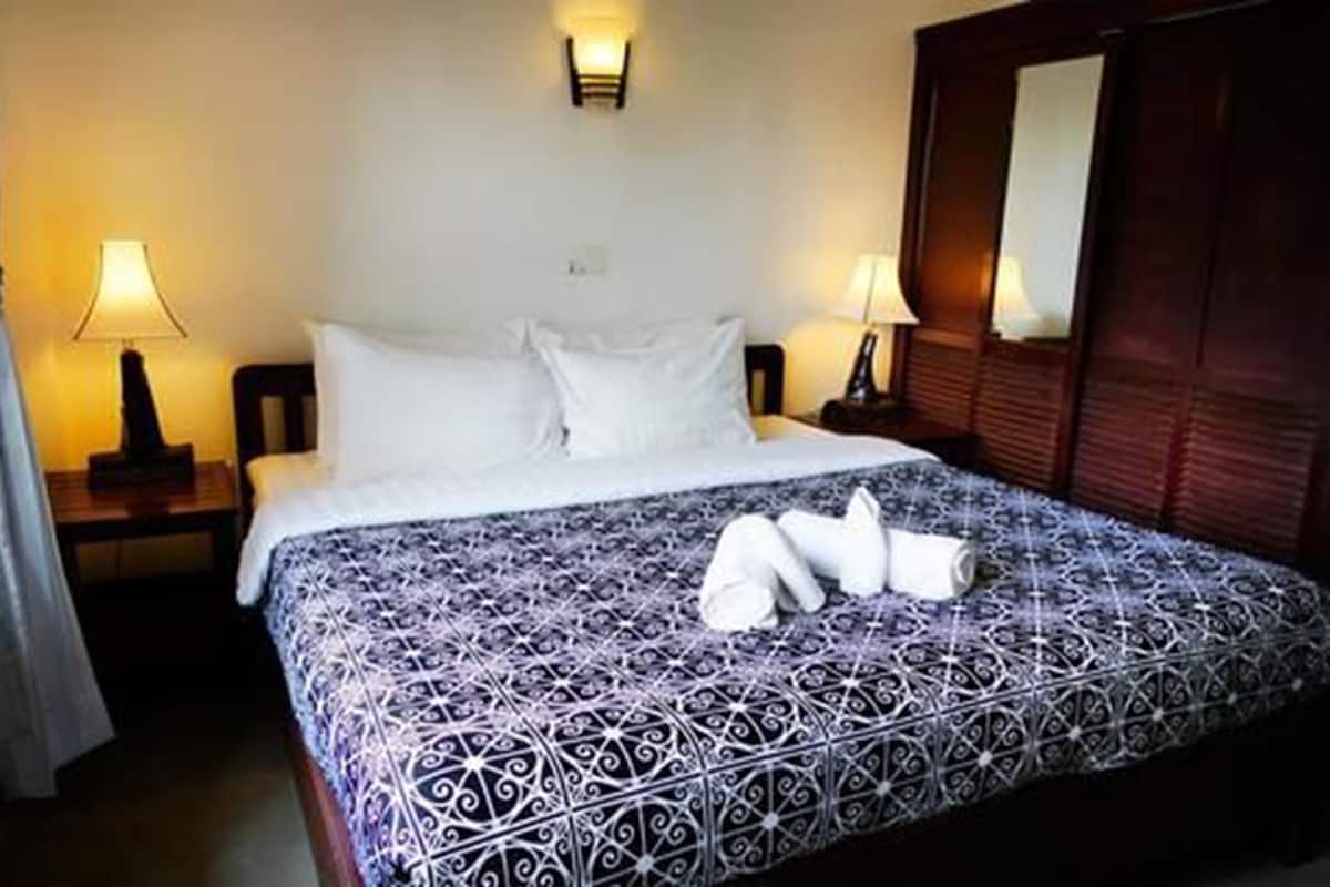 A hotel room with a large bed, two bedside tables with lamps, a wooden wardrobe, and a mirror.