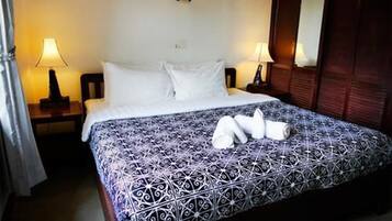 Una habitación de hotel con una cama grande, dos mesitas de noche con lámparas, un armario de madera y un espejo.