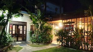 A well-lit building with a glass door entrance, surrounded by lush greenery and a paved pathway leading to the entrance. - Uncle Sam Villa (Siem Reap)