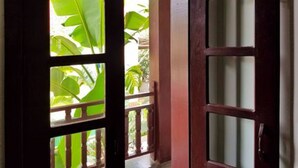 A wooden door with glass panels, leading to an outdoor area with green foliage. - Uncle Sam Villa (Siem Reap)