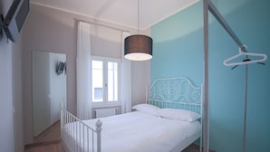 Un dormitorio con una cama blanca, una lámpara colgante, un radiador blanco y una ventana con cortinas.