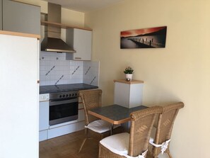 Een kleine keuken met een fornuis, oven en een eettafel met rieten stoelen.
