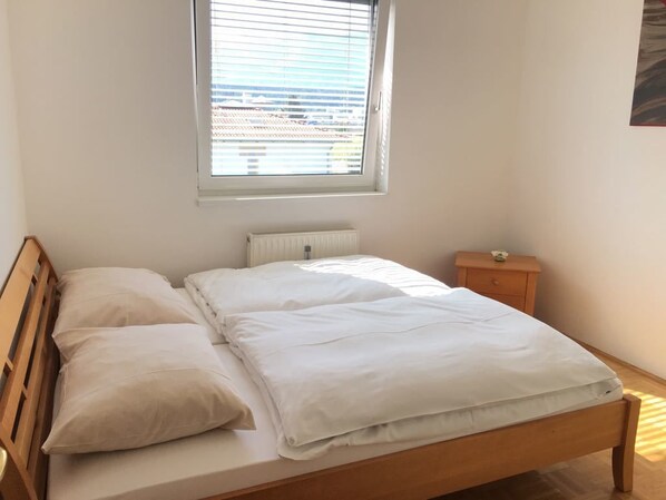 Een slaapkamer met een eenpersoonsbed, nachtkastje, raam met zonwering en een radiator.