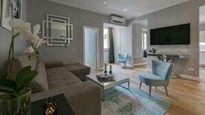 Un soggiorno moderno con divano, tavolino e poltrone. C'è una TV montata a parete e una porta che dà su un'altra stanza.