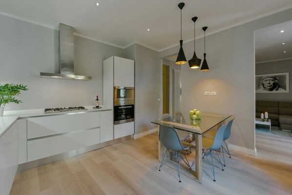 A modern kitchen with white cabinetry, stainless steel appliances, and a glass dining table with chairs.
