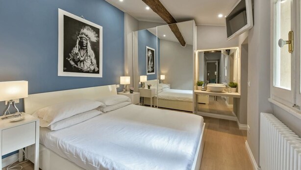 Una camera da letto con un letto grande, comodini, uno specchio, una televisione e una finestra.