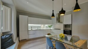 Una cucina moderna con mobili bianchi, un tavolo da pranzo in vetro e lampade a sospensione nere.