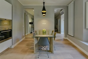 A modern kitchen with a built-in oven, a dining area with a glass table and chairs, and a pendant light above the table.