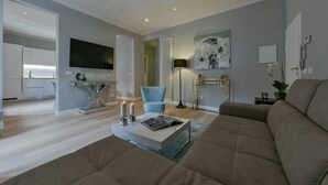 Un soggiorno moderno con un divano color beige, un tavolino da caffè con candele, una poltrona blu e un quadro appeso al muro.