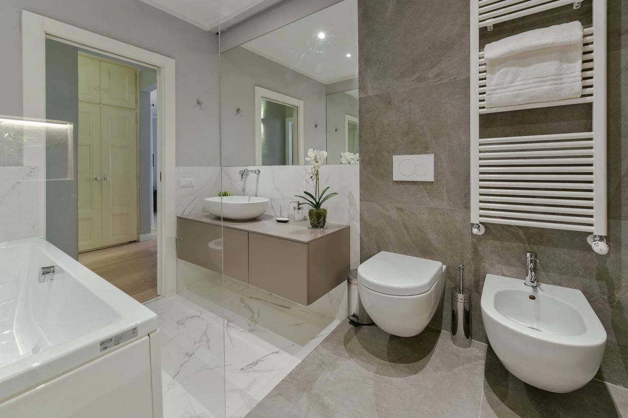 A modern bathroom with a large mirror, a sink, a bidet, and a towel rack.