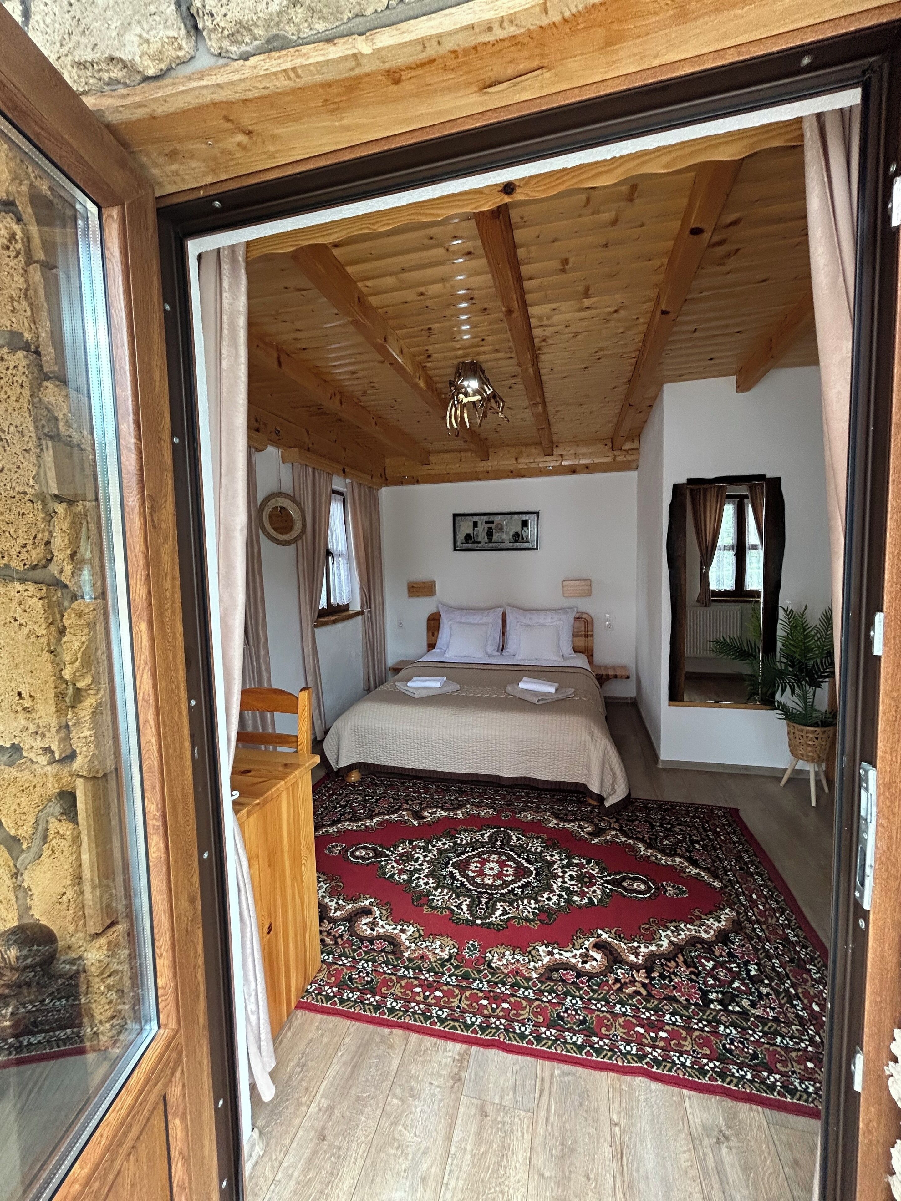 A bedroom with a wooden ceiling, a bed with a patterned rug, and a stone wall.