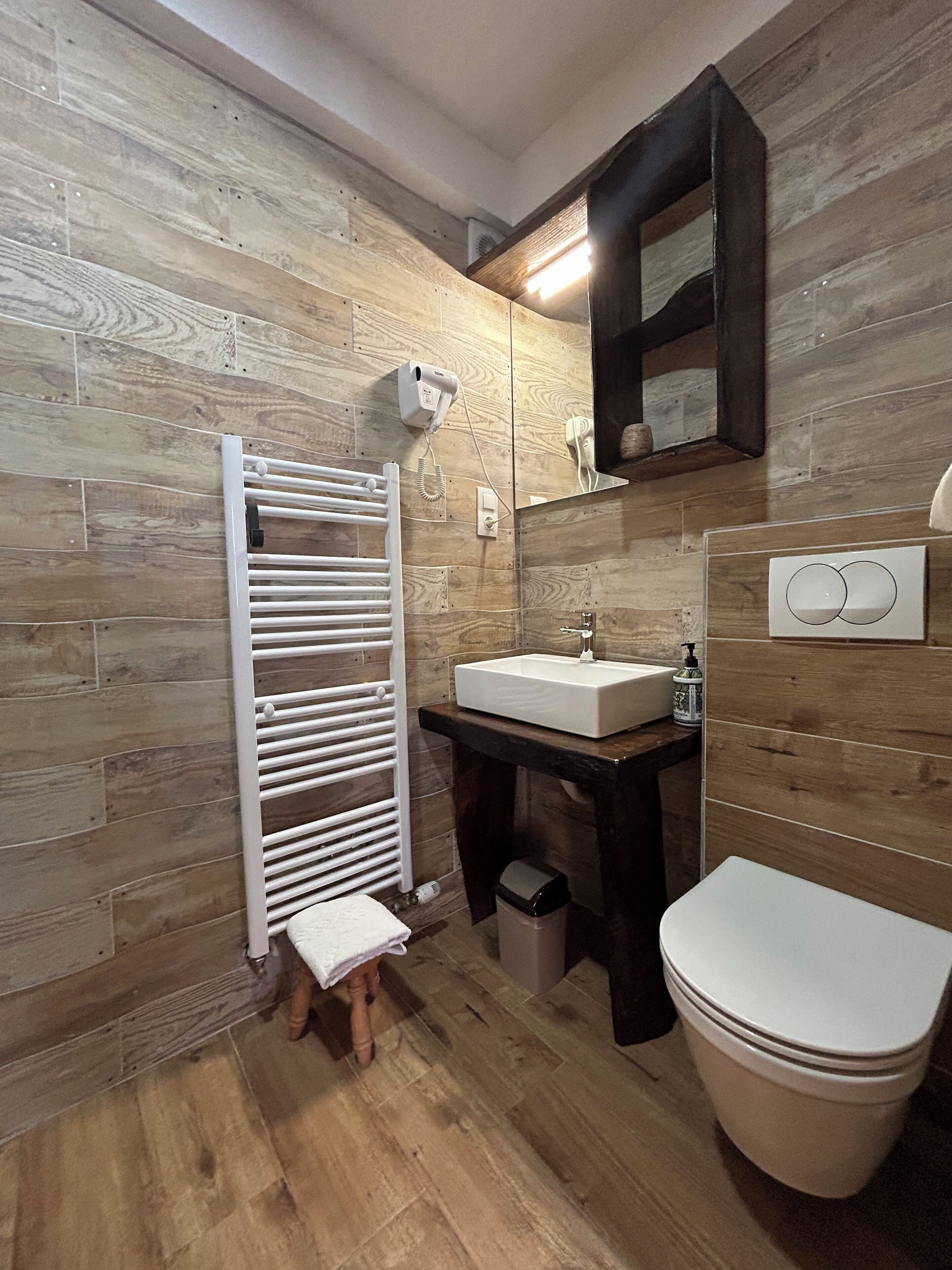 A bathroom with a wooden floor, a white toilet, a sink with a mirror above it, and a towel rack.