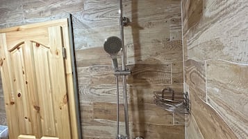Une douche équipée d’un pommeau de douche à main et d’une douchette à pluie fixée au mur, une porte en bois et un mur en bois avec un motif de planches.