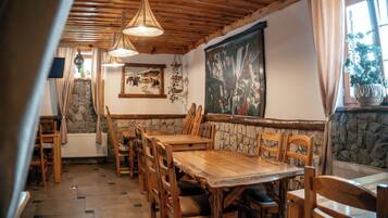 A dining area with wooden tables and chairs, a stone wall, and a large painting on the wall.