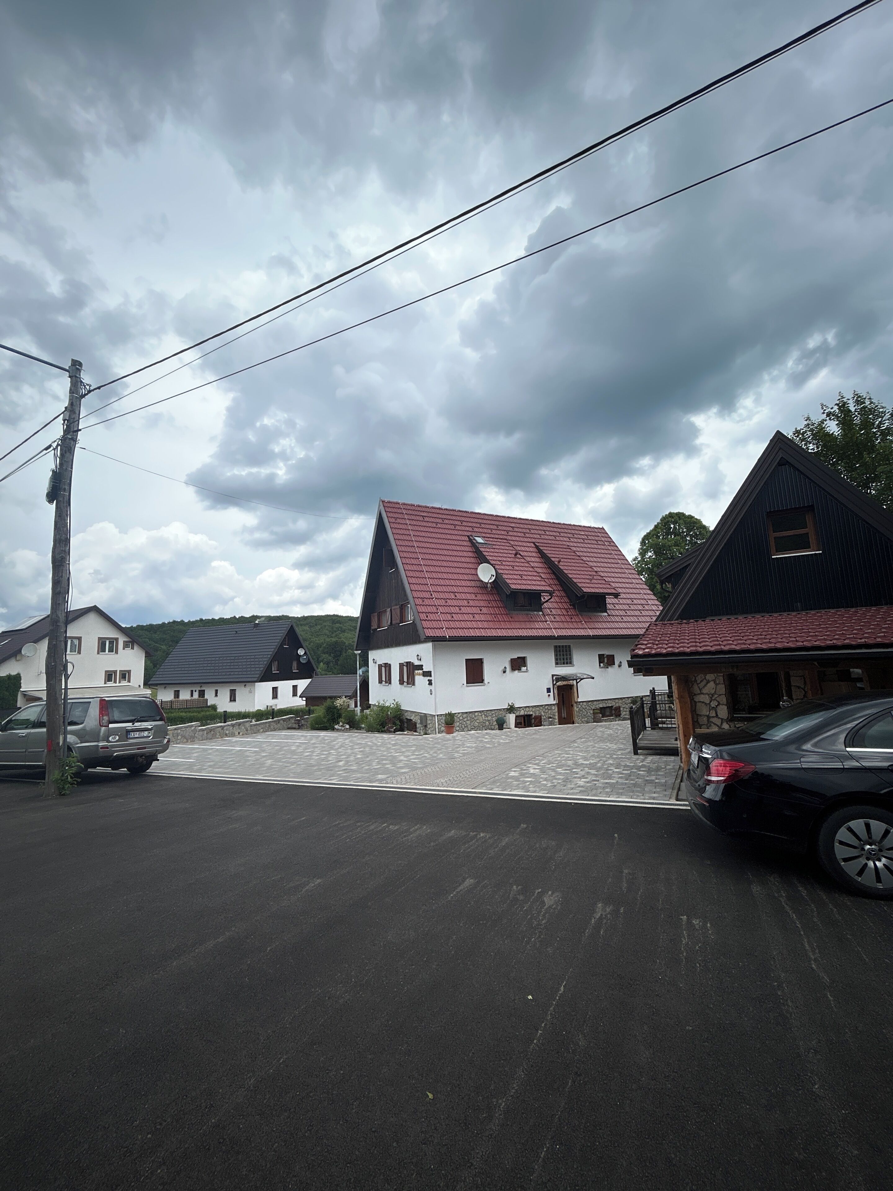 A residential area with houses, a paved driveway, and parked cars.