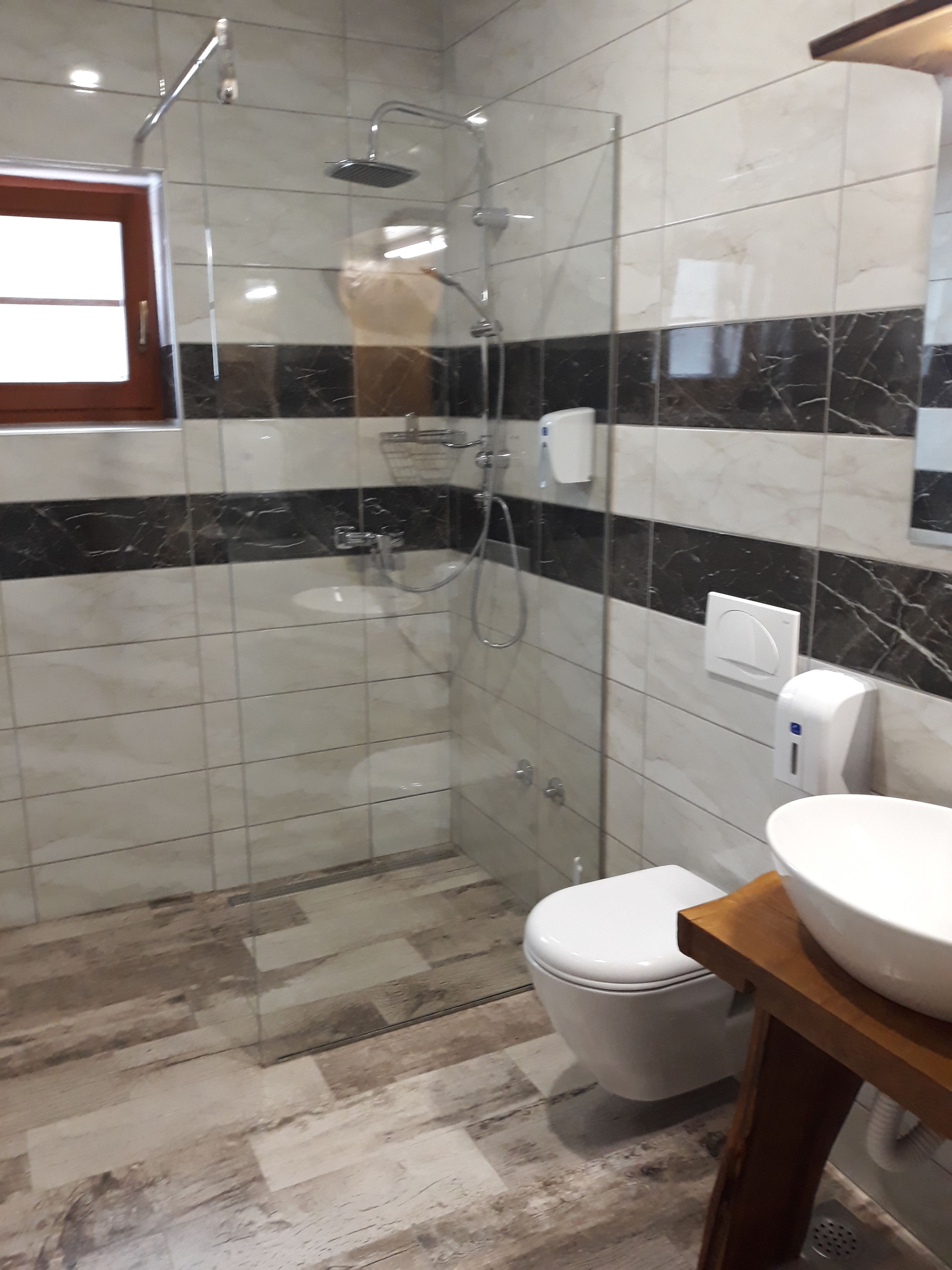 Une salle de bain avec une douche à parois de verre, des toilettes blanches et un meuble-lavabo en bois doté d’un grand évier.