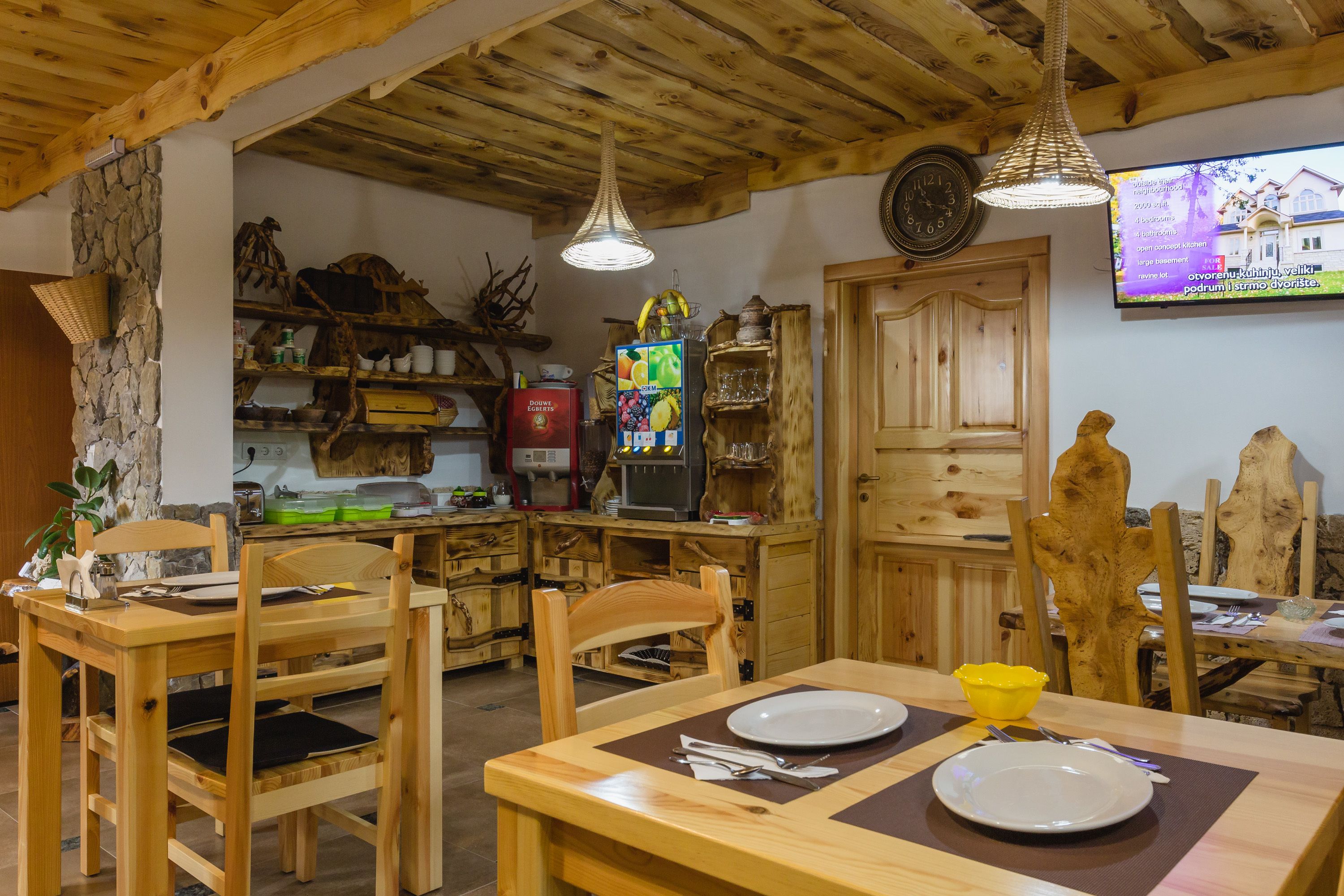A rustic wooden dining area with a stone wall, wooden chairs, a wooden table, and a television mounted on the wall.
