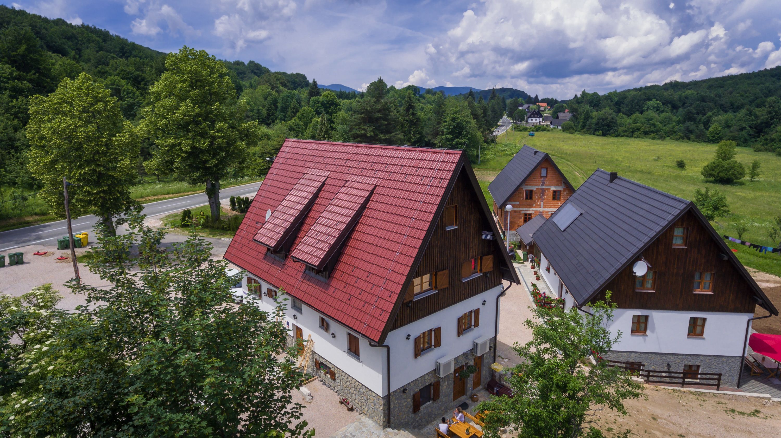 A traditional wooden house with a red roof, a stone foundation, and a small porch with outdoor seating.