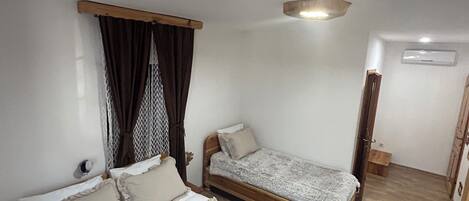 A bedroom with two beds, a wooden headboard, a ceiling light, and a small wooden cabinet.