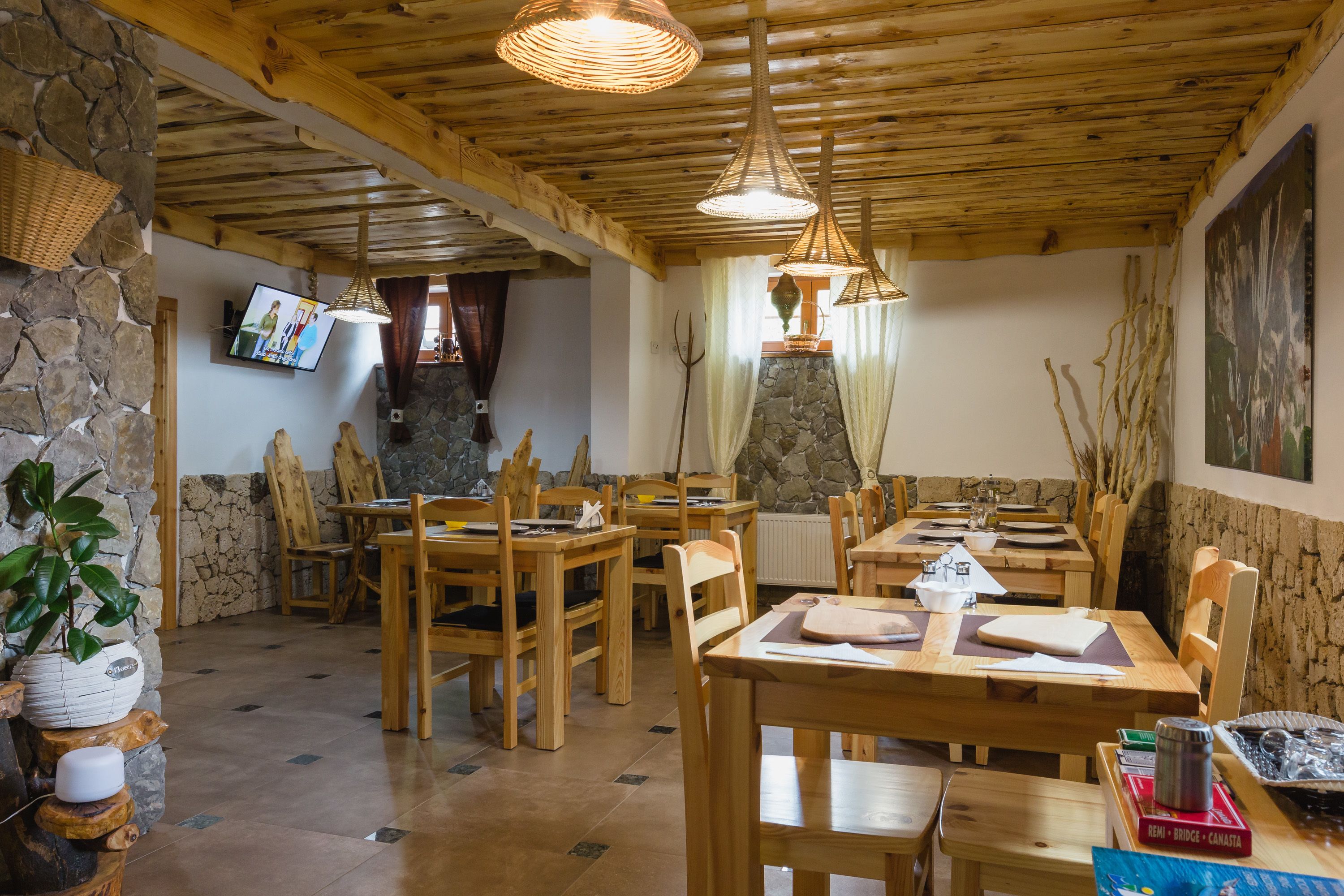 A rustic dining area with wooden tables and chairs, stone walls, and a television mounted on the wall.