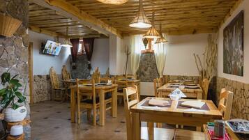 A rustic dining area with wooden tables and chairs, stone walls, and a television mounted on the wall.