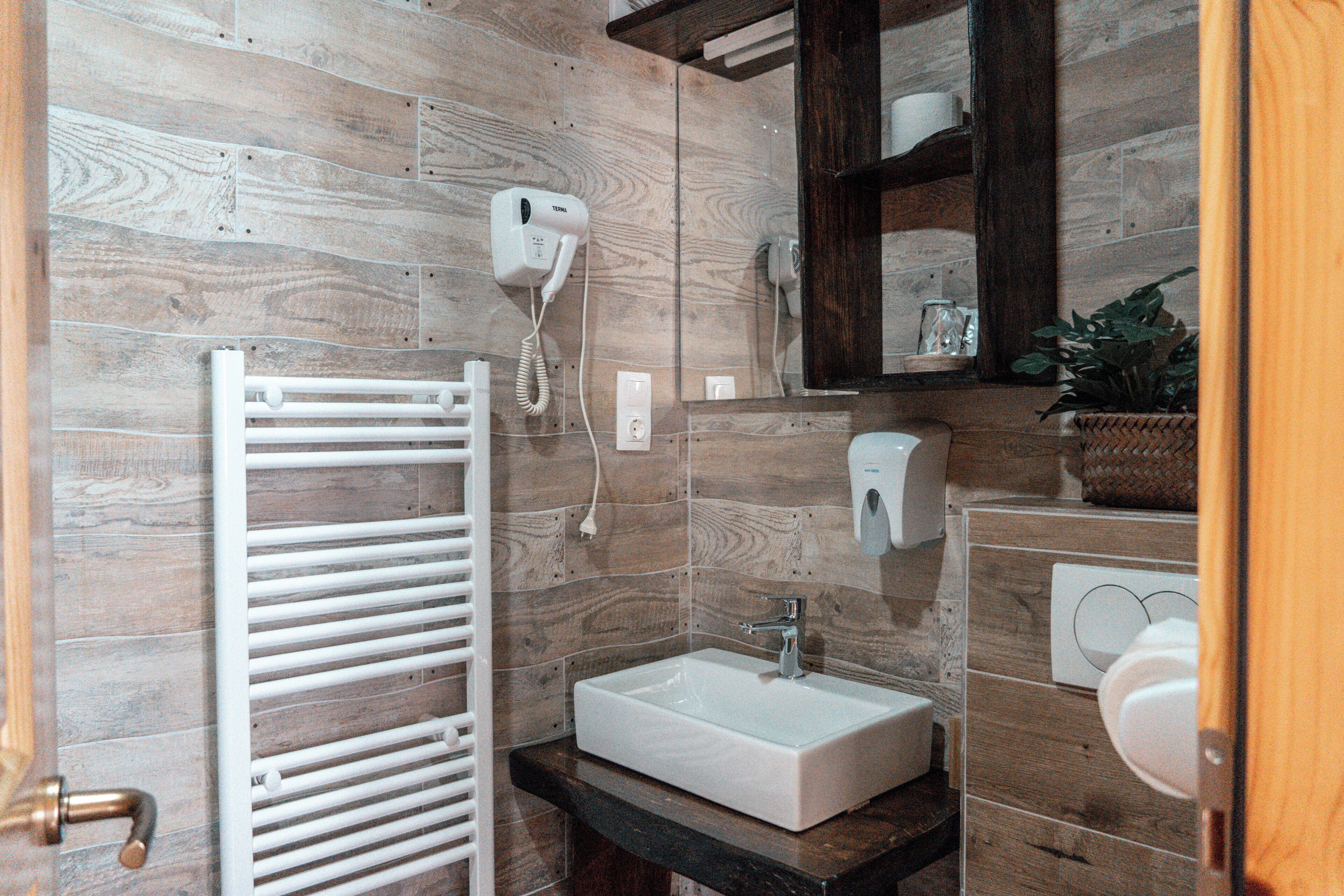 Un baño con lavamanos blanco, toallero, espejo y secador de pelo montado en la pared.