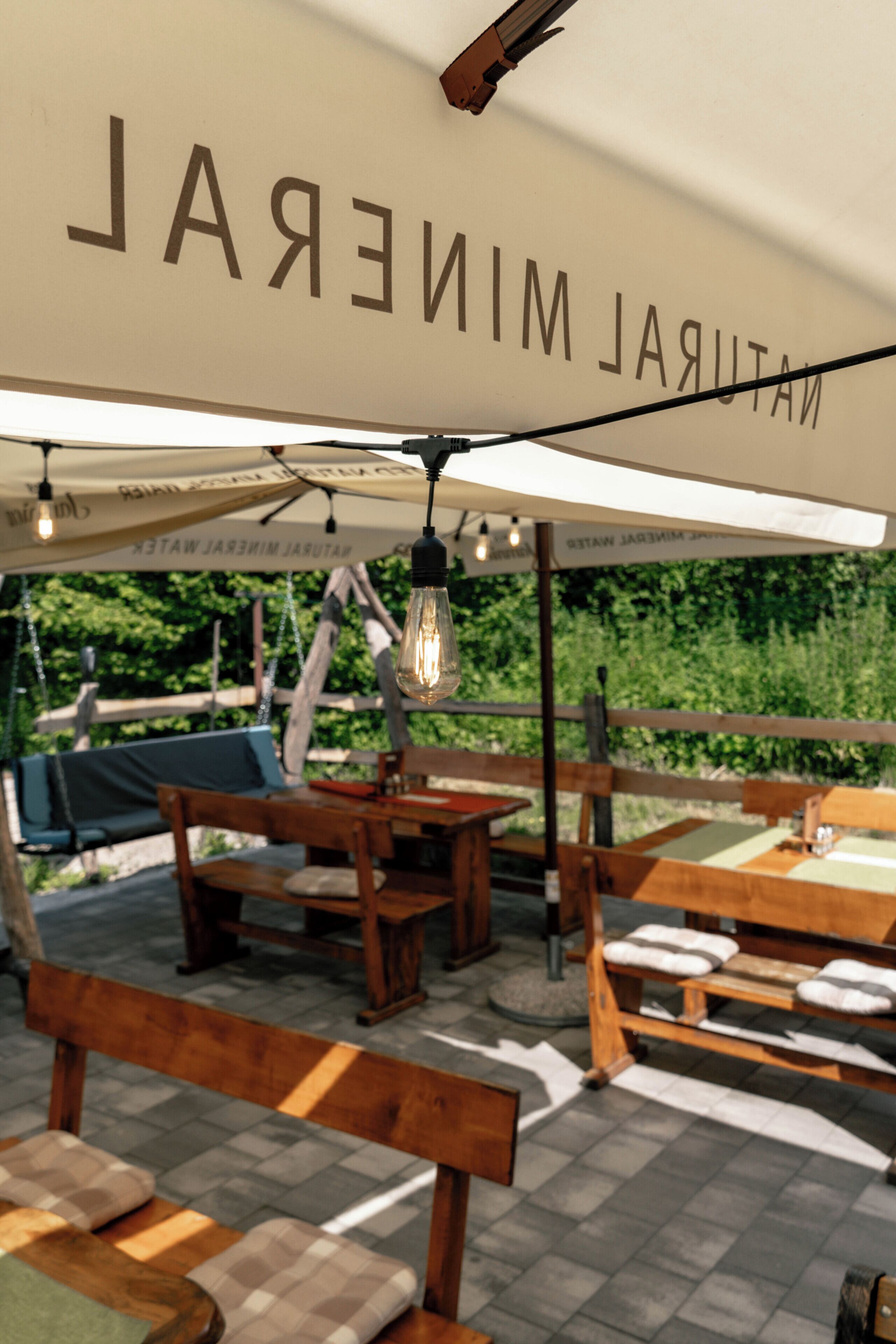An outdoor seating area with wooden tables and benches, under a canopy with the text 'NATURAL MINERAL WATER'.