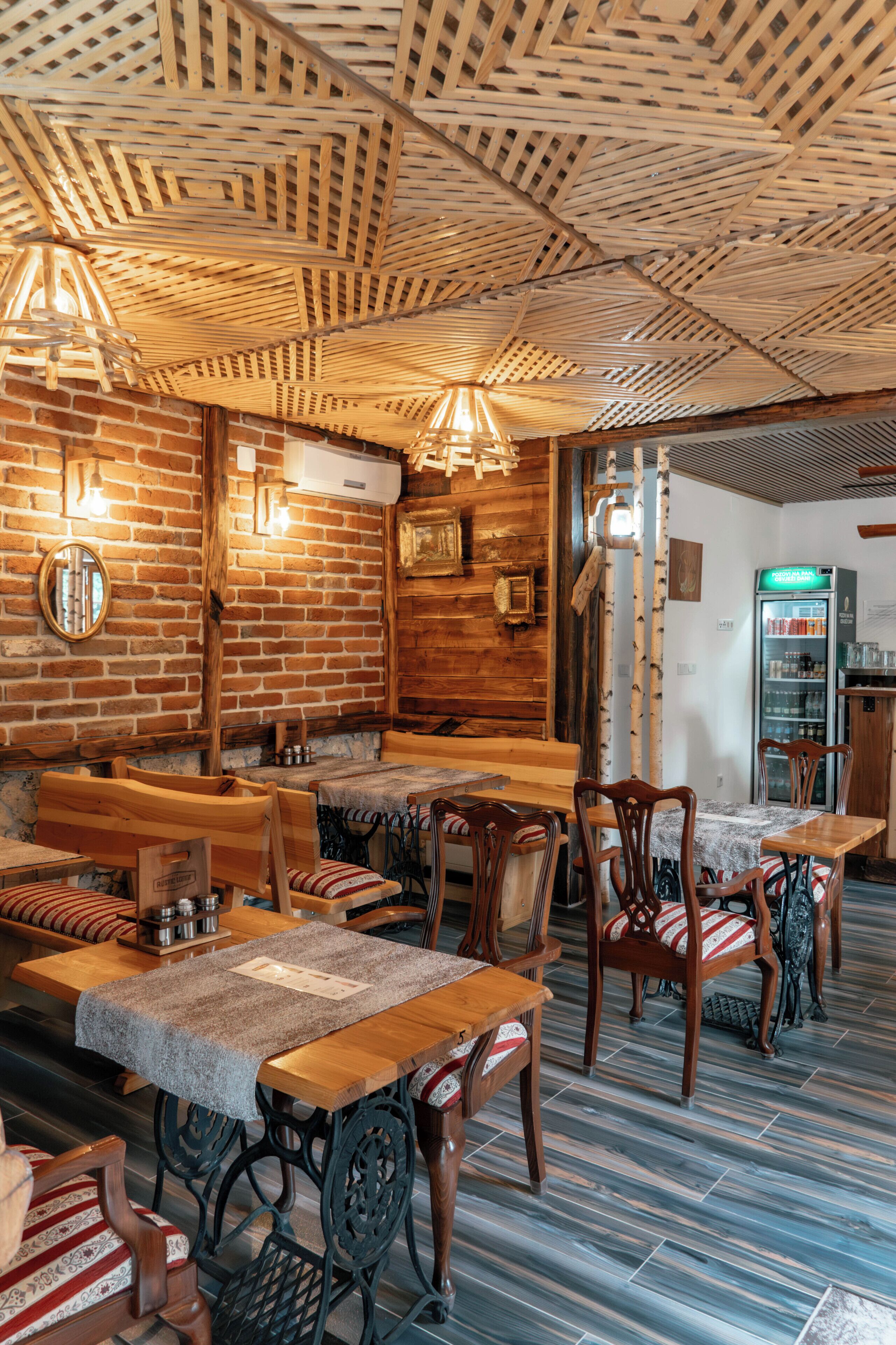 A restaurant interior with brick walls, wooden tables and chairs, and a patterned ceiling.