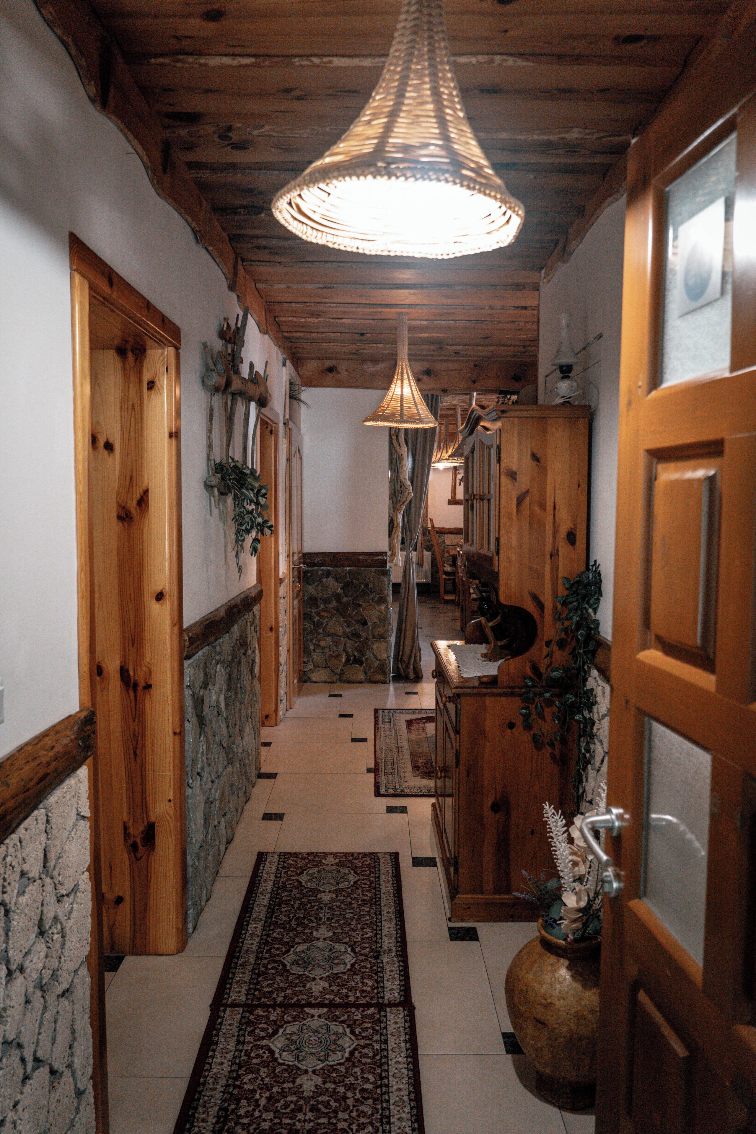 Un corridoio con porte in legno, un muro in pietra, un tappeto decorato e un lampadario.