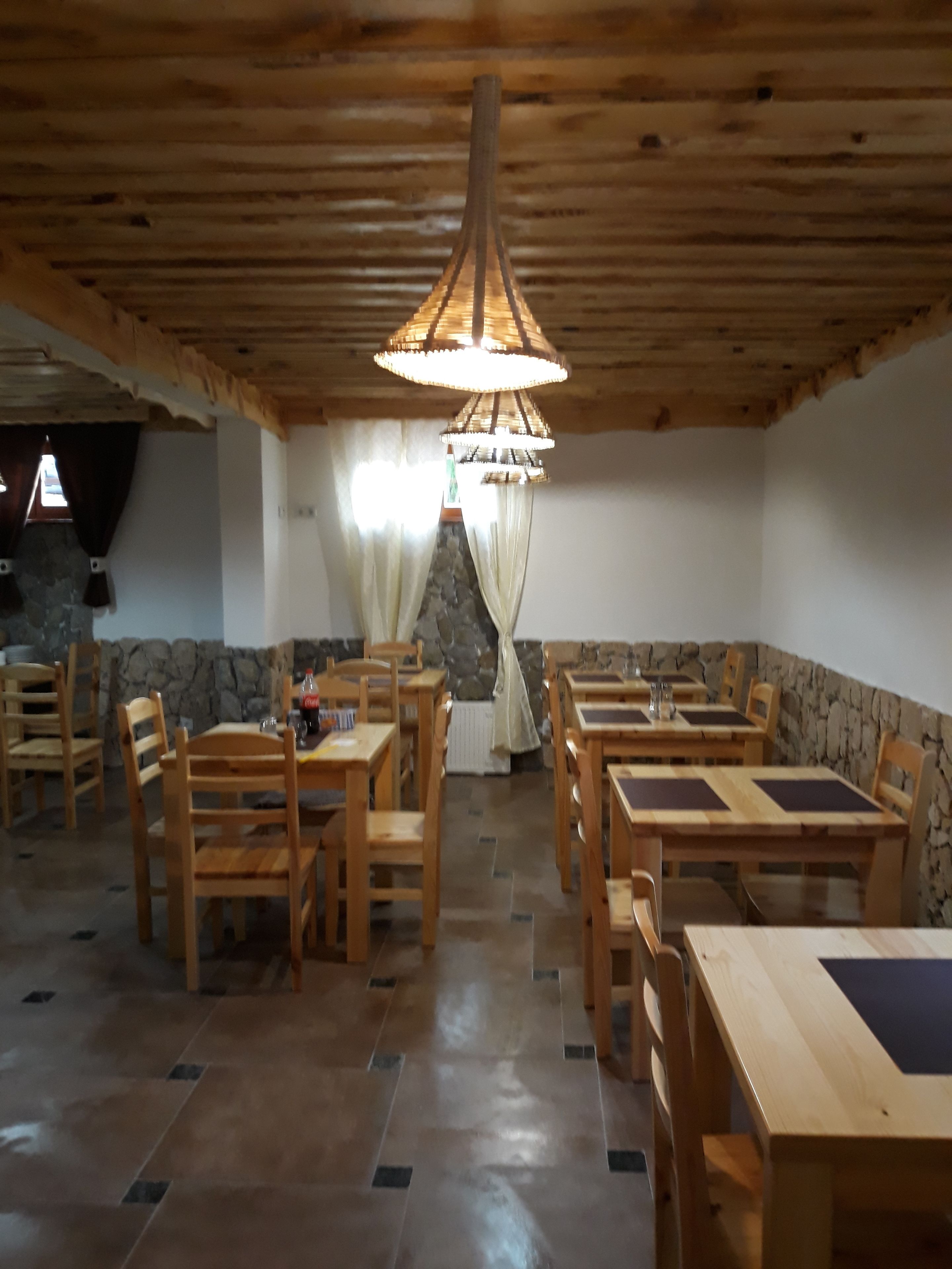 A rustic dining area with wooden tables and chairs, a stone wall, and a hanging light fixture.