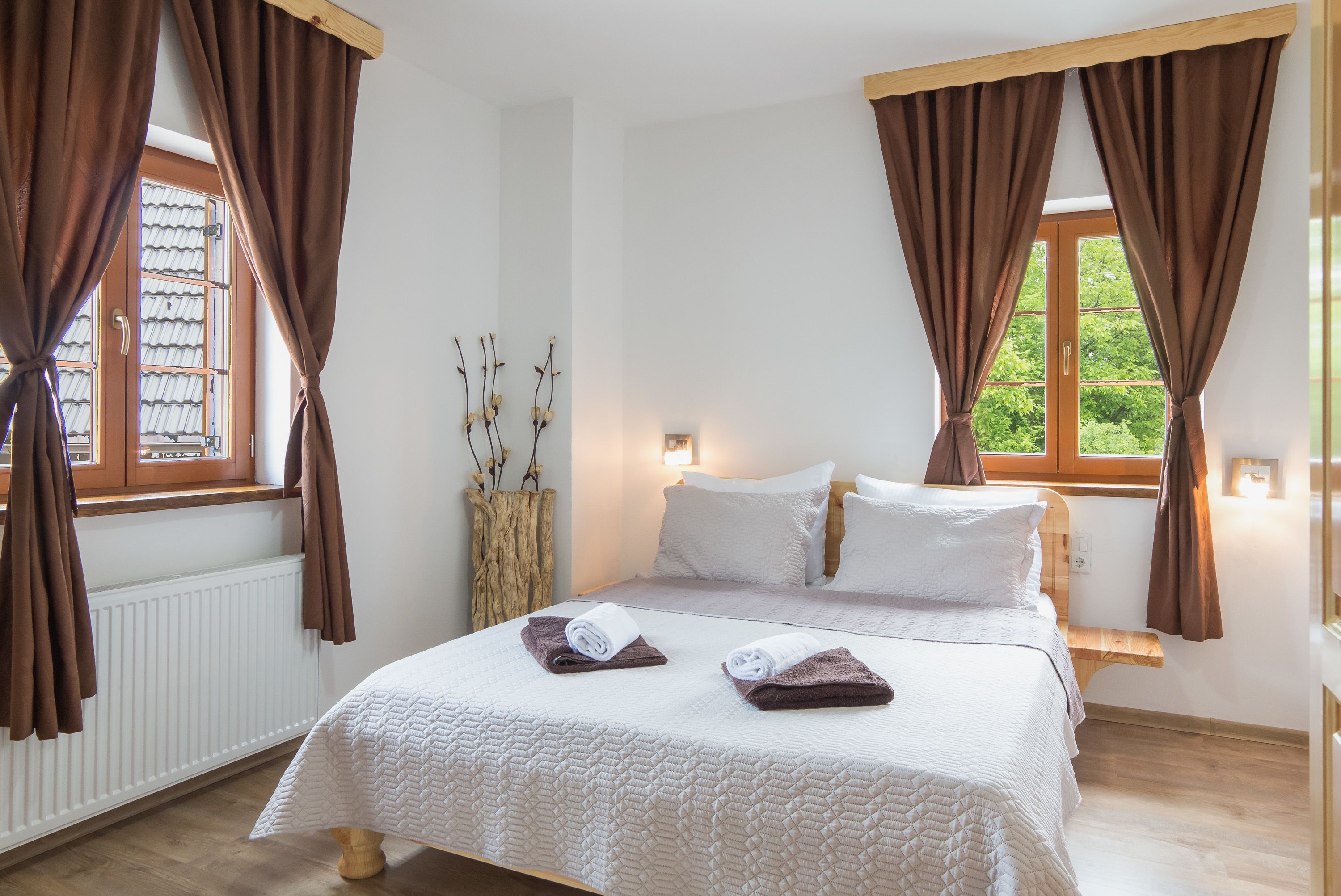 A bedroom with a bed, two windows, a radiator, and a bedside table.