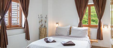 A bedroom with a bed, two windows, a radiator, and a bedside table.