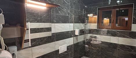 A modern bathroom with a marble backsplash, a wooden vanity, a white sink, a toilet, and a shower area.