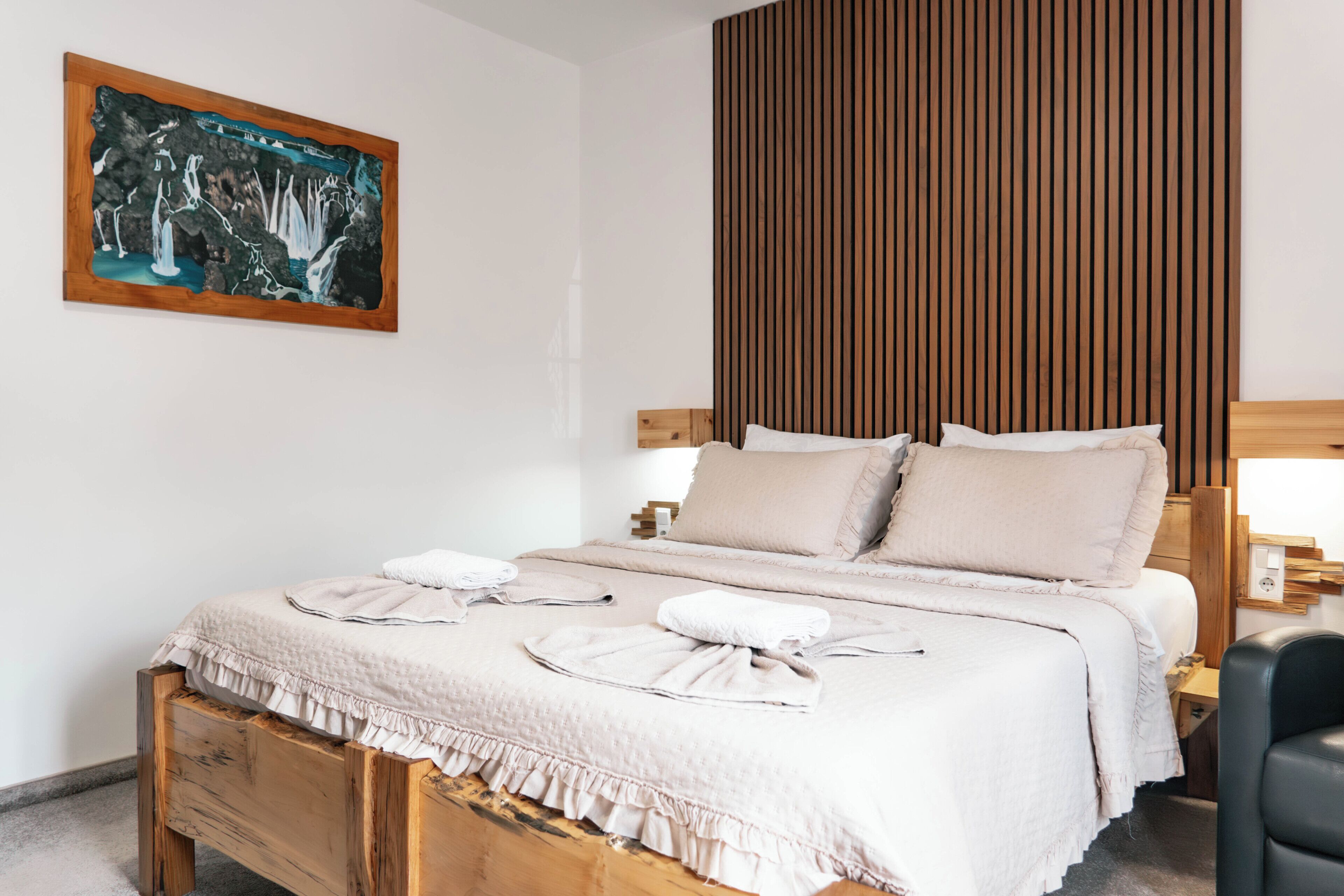 A bedroom with a wooden bed, a painting on the wall, and a wooden panel wall.