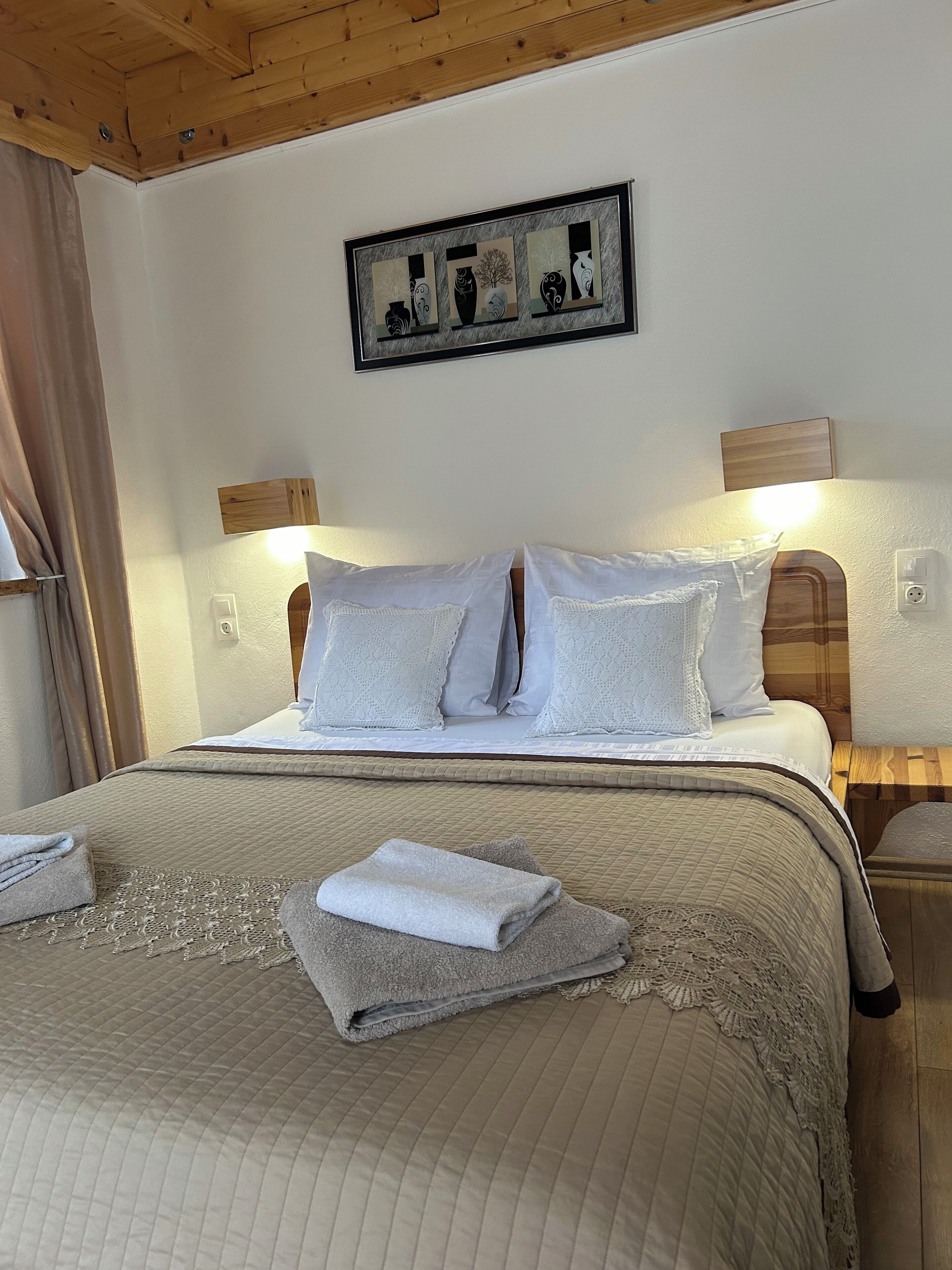 A neatly made bed with a quilted bedspread, two pillows, and a folded towel on the bed. There is a framed artwork above the bed and a wooden headboard.