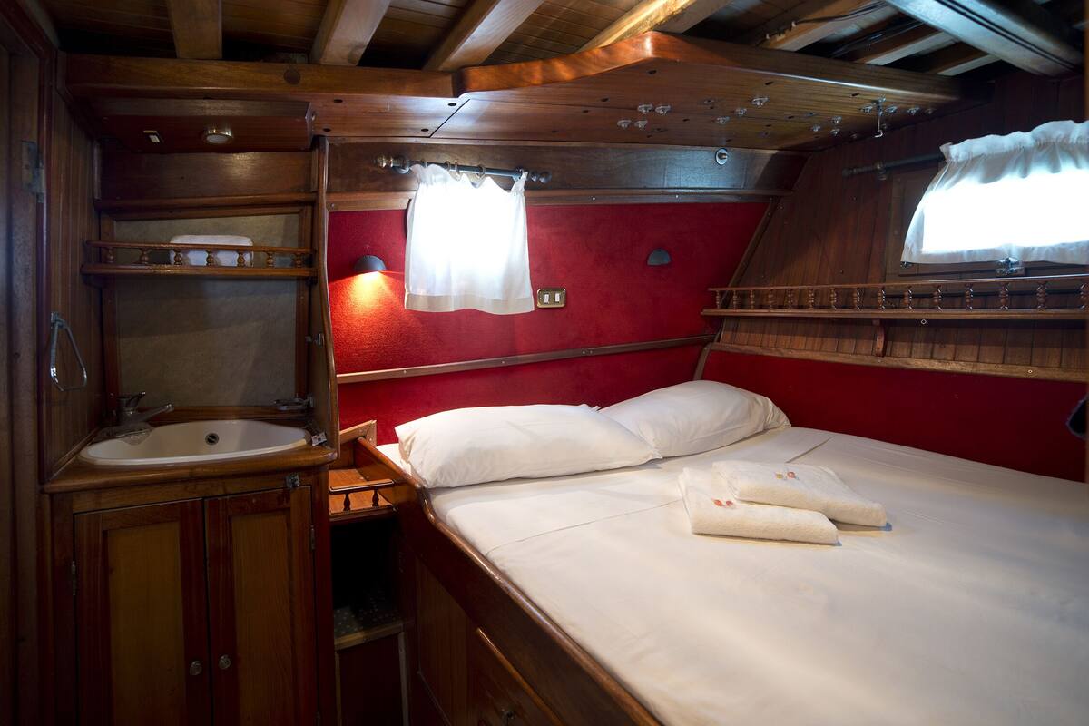 A compact cabin with a wooden interior, a single bed with white linens, a small sink, and a window with curtains.
