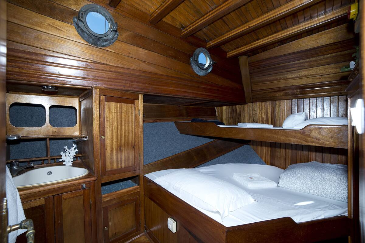 A compact cabin with a wooden interior, a bunk bed, a small sink, and a mirror.