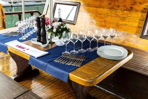 A table set for a meal with wine glasses, plates, and cutlery, on a wooden deck with a view of water. - Caicco Akos (Venice)