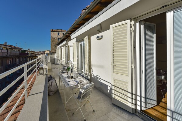 A balcony with a table set for dining, white shutters, and a view of the cityscape.