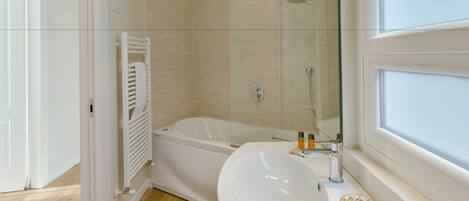 Un baño moderno con cabina de ducha de vidrio, una bañera blanca y un lavabo grande con un objeto de vidrio decorativo en la encimera.