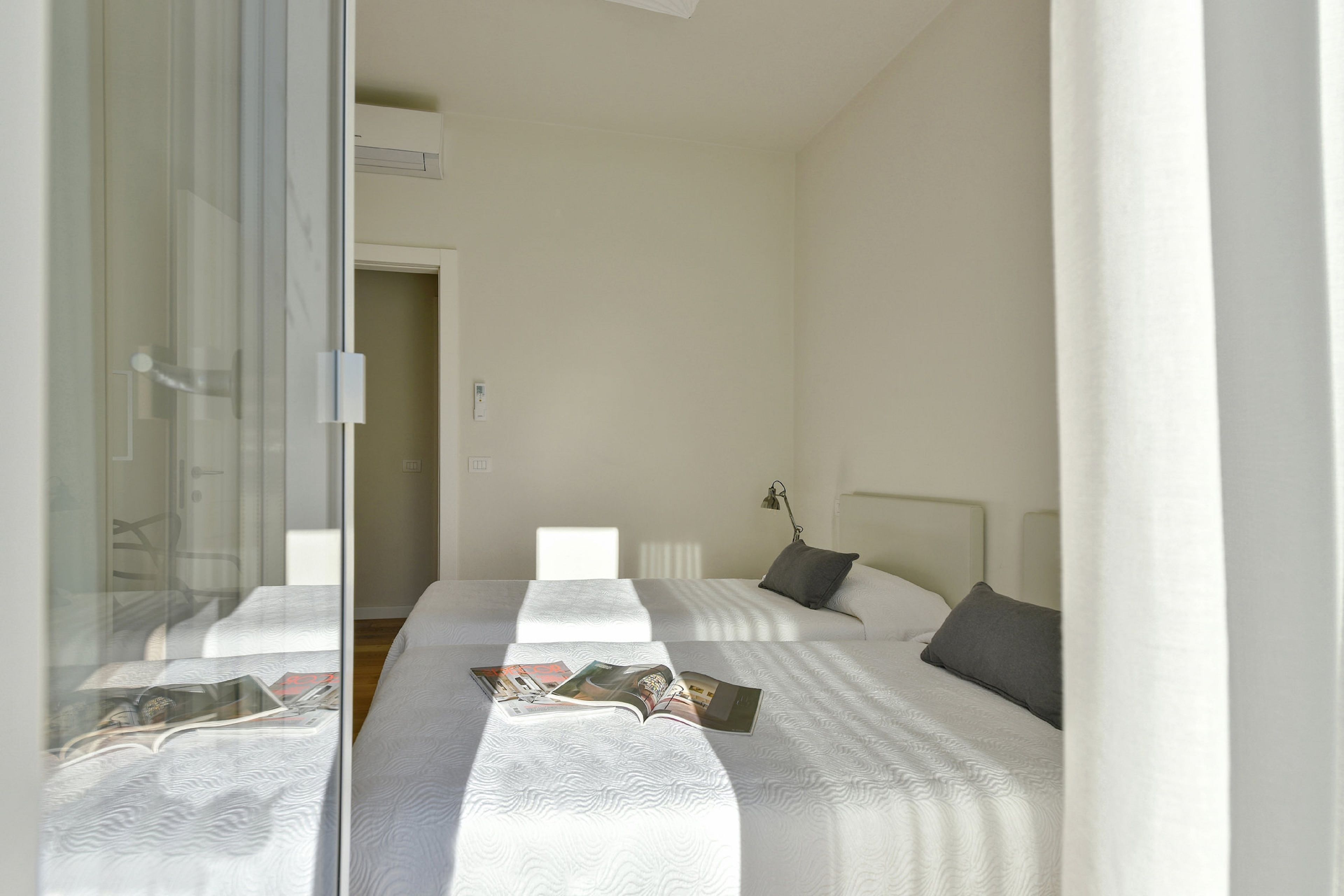 Hotellihuone, jossa on kaksi sänkyä, lasiovi ja yöpöytä, jossa on lamppu.