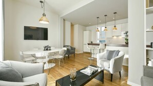 Una sala de estar moderna con comedor, cocina y un ventanal que deja entrar mucha luz natural.
