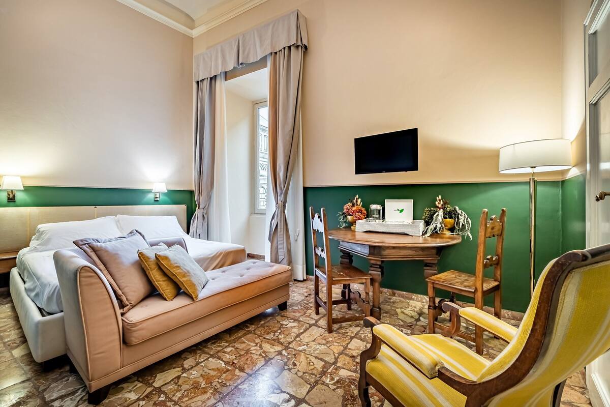 Een hotelkamer met een bed, een slaapbank, een bureau met een computer, een stoel en een televisie.