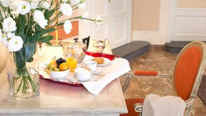 Un plateau de petit-déjeuner avec des fruits, une tasse et un muffin, posé sur une table agrémentée d’un vase de fleurs.