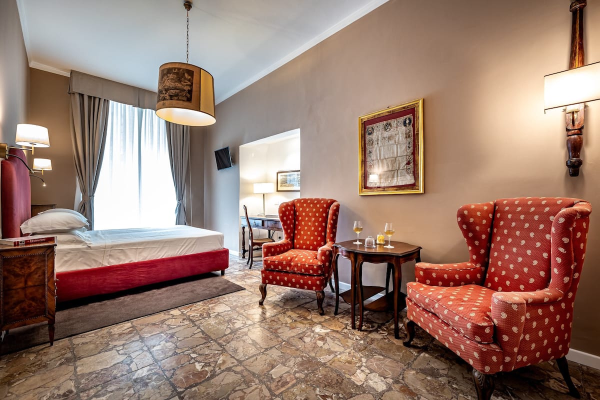 Een hotelkamer met een bed, twee fauteuils, een tafeltje, een lamp en een schilderij aan de muur.